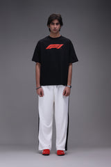 Person wearing a black t-shirt with a Formula 1 red logo and white pants and red speedcat puma shoes on a gray background