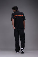 Person wearing a boxy fit black t-shirt with an orange Mclaren formula 1 team logo showing backside of the shirt