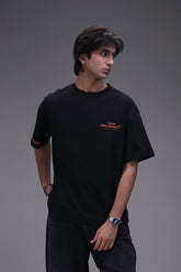 Person wearing a boxy fit black t-shirt with an orange Mclaren formula 1 team logo on a gray background