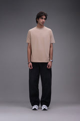 Man wearing a beige t-shirt and black pants against a gray background