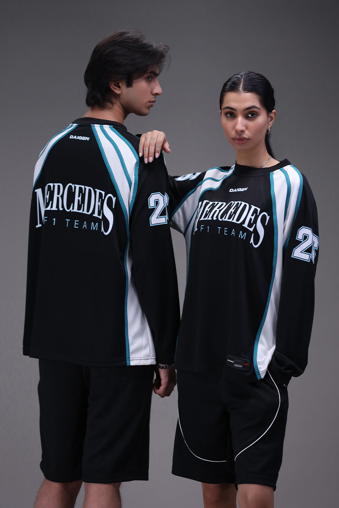 Two people wearing matching black mercedes formula 1 team sports outfits with Mercedes branding on a gray background