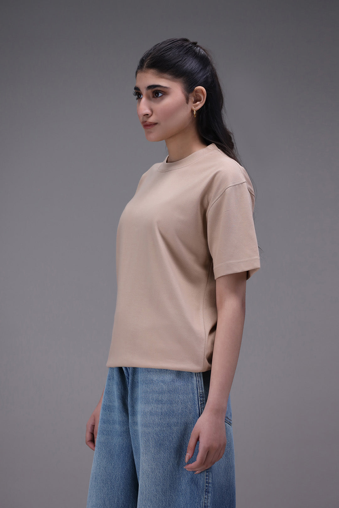 Woman wearing a beige t-shirt and blue jeans against a gray background