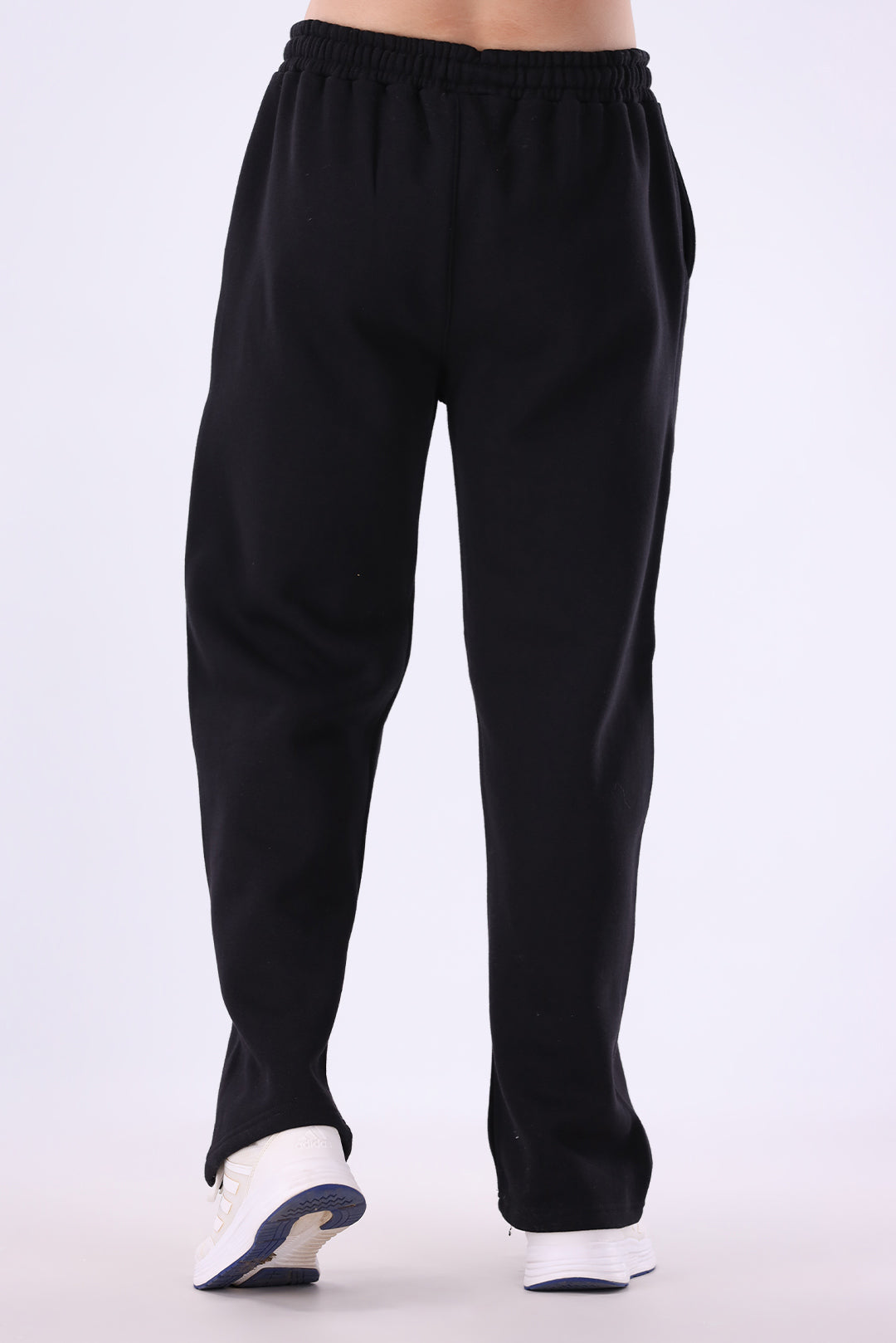 Black sweatpants with an elastic waistband, shown from the back on a model wearing white sneakers against a light gray background.