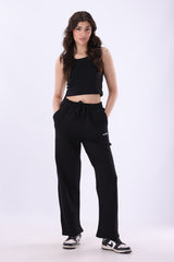 A woman modeling a black  black wide-leg sweatpants with white sneakers, standing against a plain white studio background.