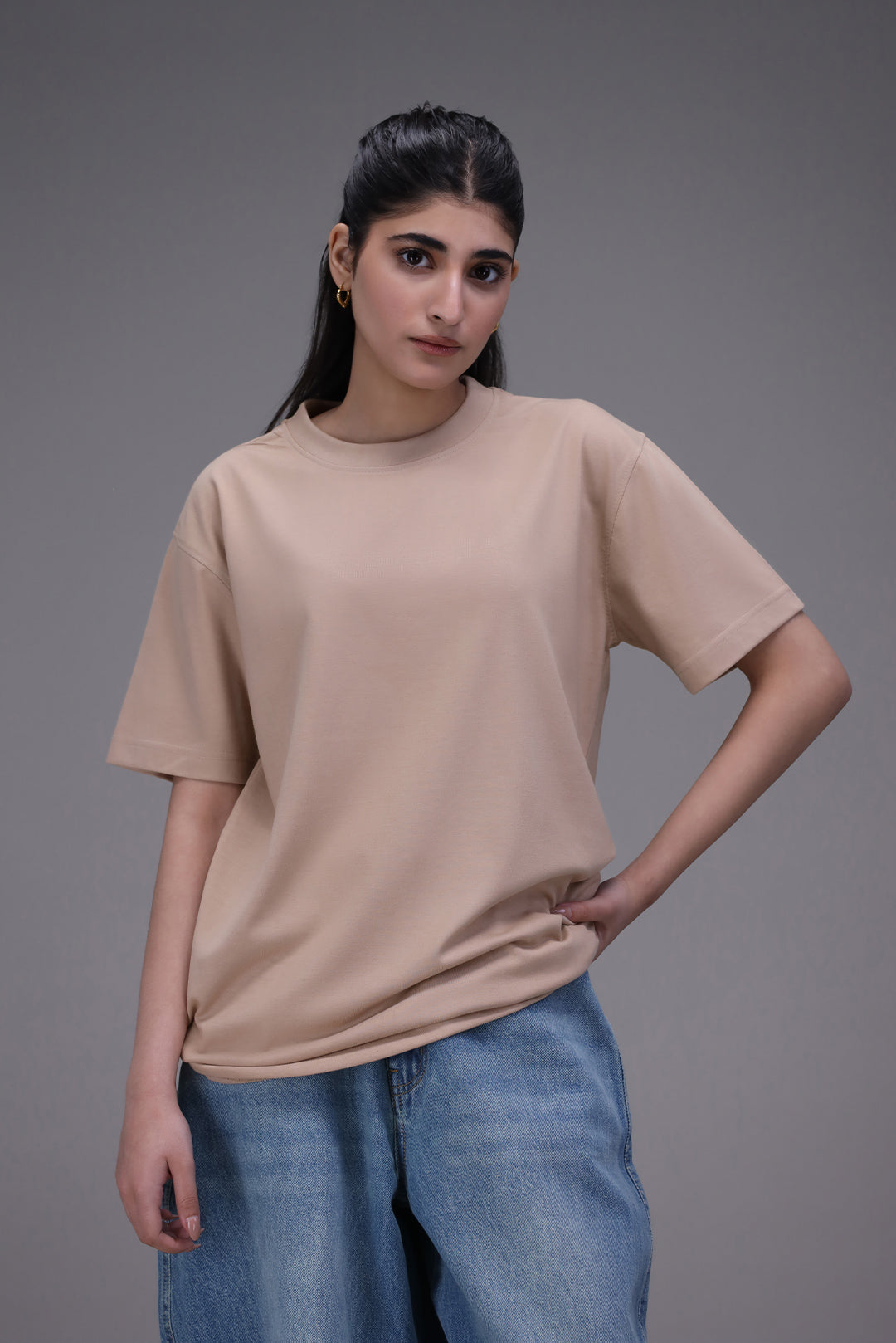 Woman wearing a beige t-shirt and blue jeans against a gray background