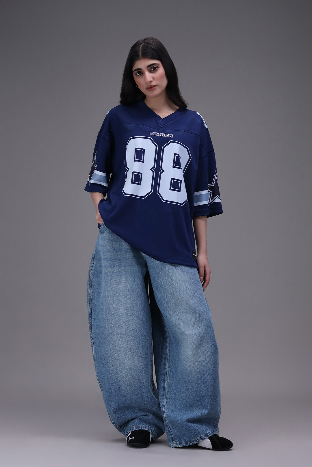 Person wearing a blue dallas cowboy lamb 88 sports jersey with the number 88 and wide-leg jeans on a gray background