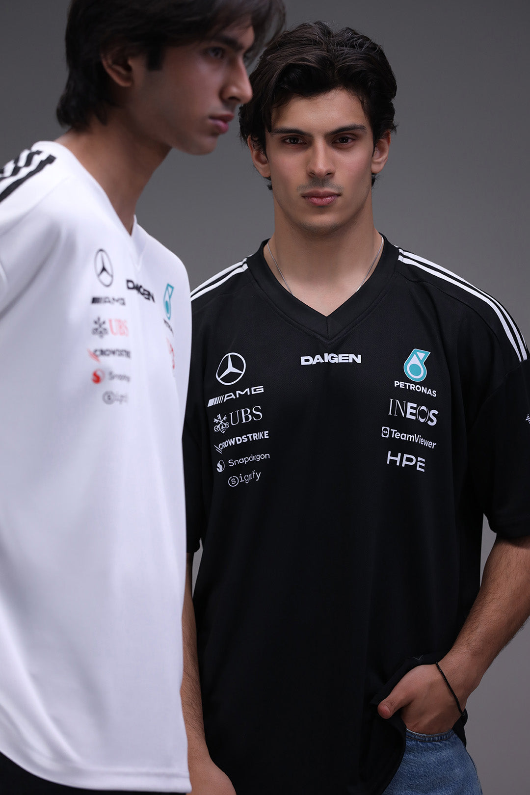 Two individuals wearing branded mercedes petronas black and white jerseys against a gray background