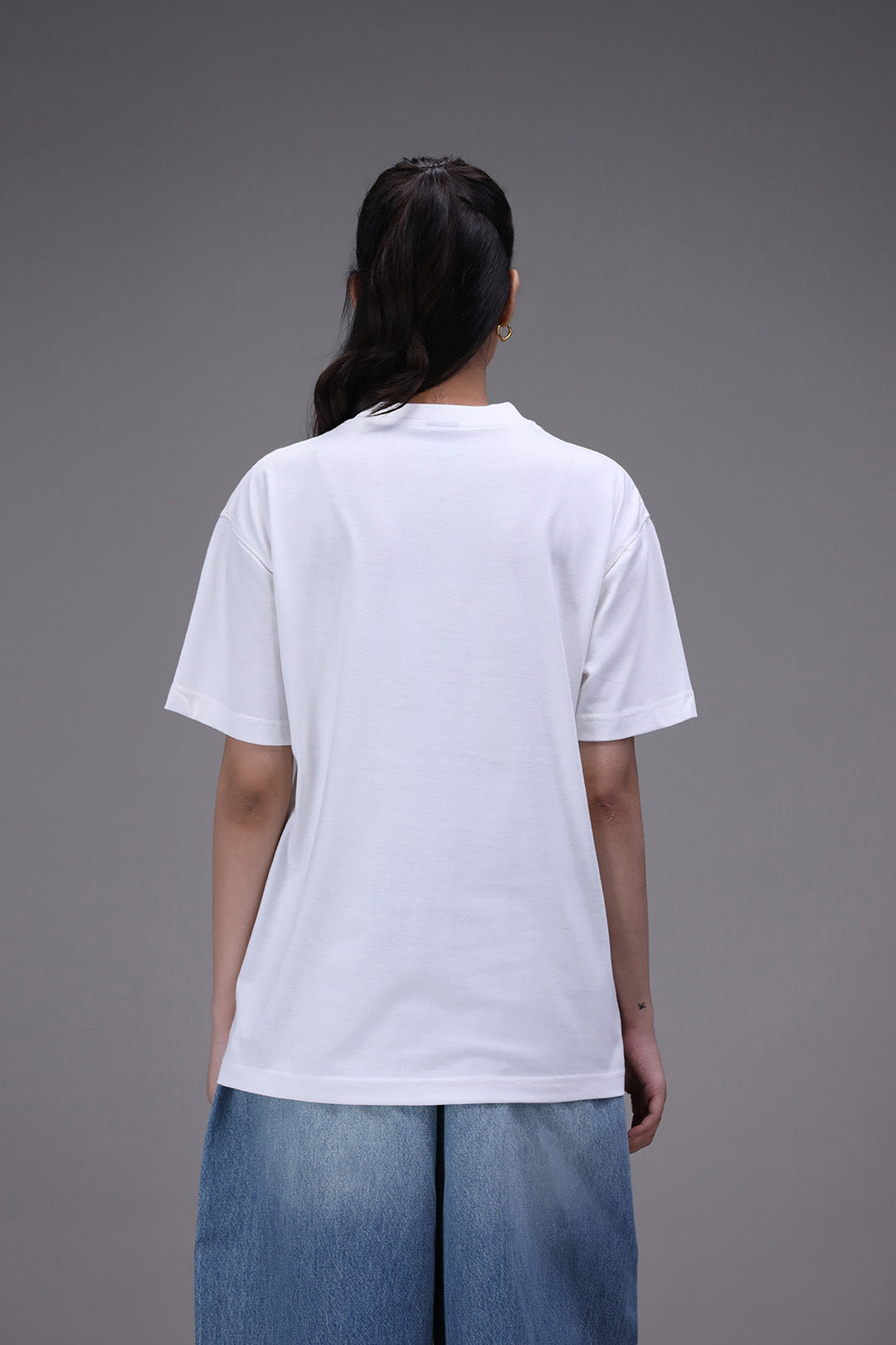 Person wearing a plain white t-shirt and blue jeans on a gray background