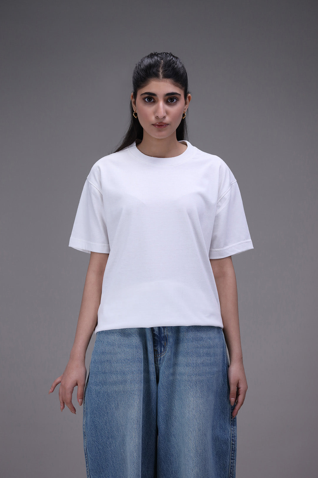 Woman wearing a plain crew neck white t-shirt and blue jeans on a gray background